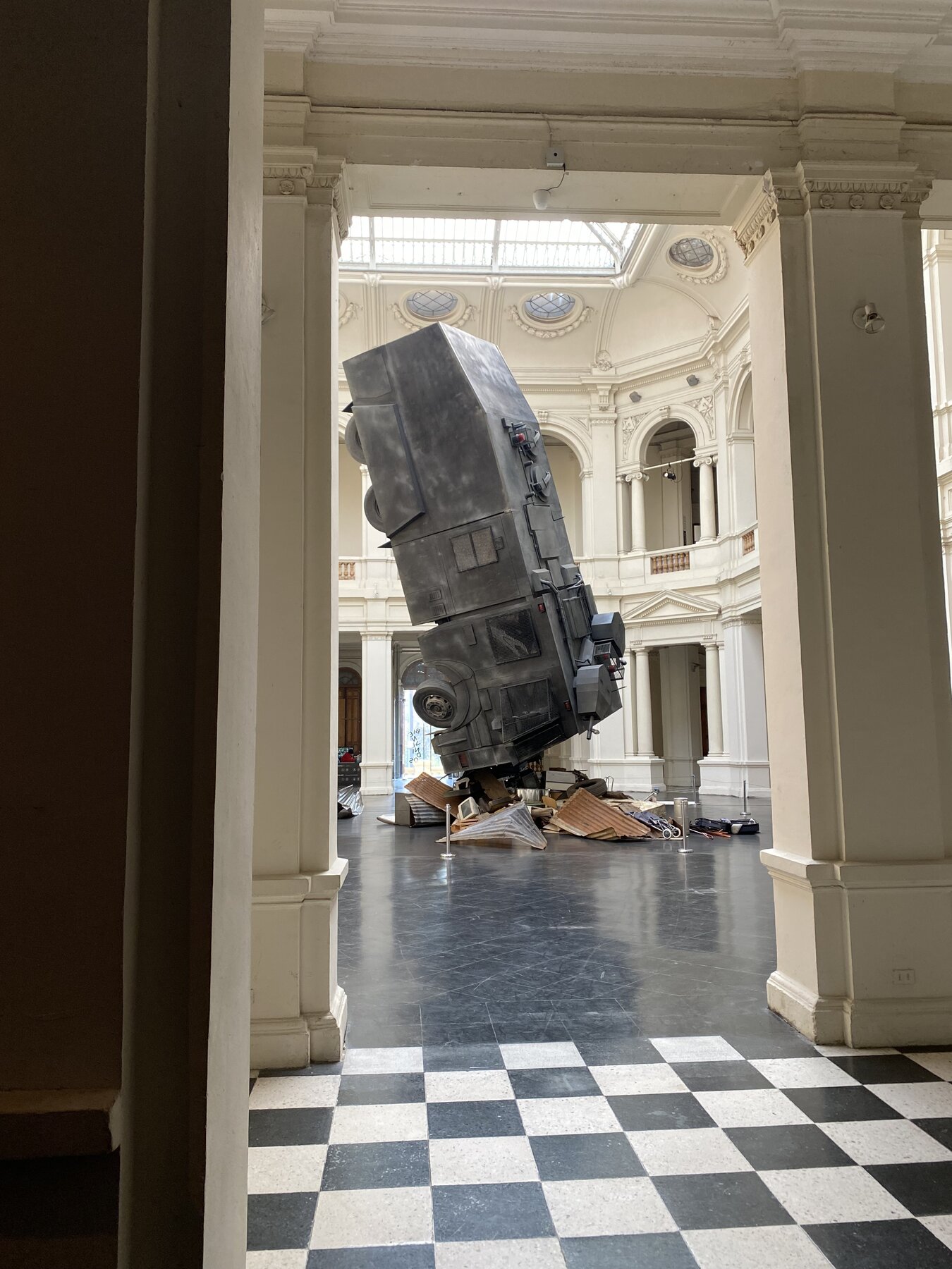 A tilted armored truck sculpture in a grand museum hall